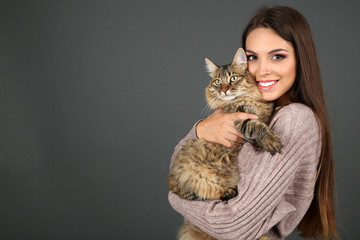 Beautiful young woman holding cat on gray background