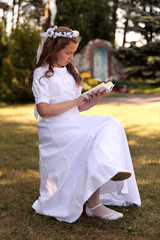 Dziewczynka w białej sukni czyta książeczkę.