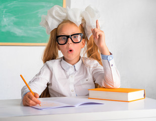The girl sits at a school desk with textbooks