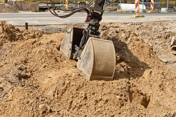 Die Doppelschaufel von einem Bagger greift in einen Sandhaufen