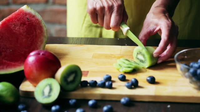 Woman cutting kiwi on the chopping board, closeup
