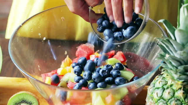 Woman mixing fruits in big glass bowl, closeup