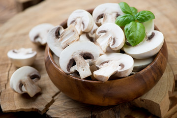 Raw sliced champignons and green basil in a wooden bowl