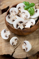 Close-up of a wooden bowl with raw champignons and green basil