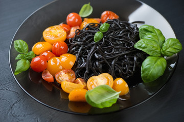 Glass plate with black tagliatelle, roasted tomatoes and basil