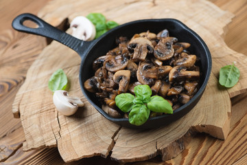 Cast-iron frying pan with roasted mushrooms over wooden surface