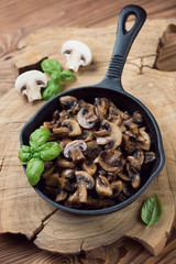 Frying pan with roasted champignons and green basil, studio shot