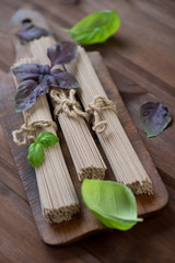 Dry buckwheat noodles with basil over rustic wooden background