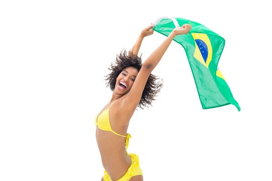 Fit girl in yellow bikini holding brazil flag laughing at camera