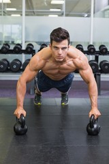 Fototapeta na wymiar Muscular man doing push ups with kettle bells in gym