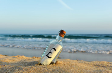 Obraz premium British pound in a bottle on the beach