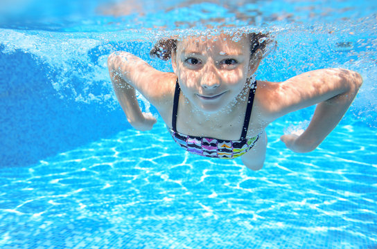 Happy underwater child swims in pool, girl swimming