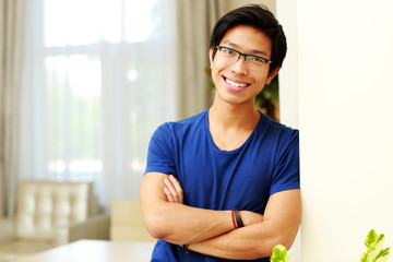 Cheerful asian man standing with arms folded at home