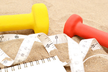 Notebook and dumbbells on sand