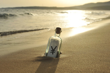 Yen, currency of Japan in a bottle on the beach, rising sun