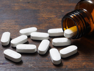 Pills spilling out of a pill bottle on wooden table
