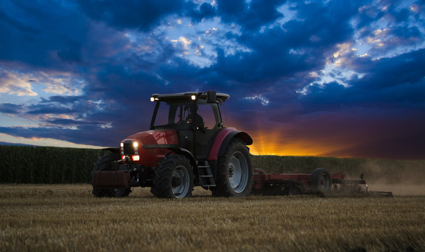 Tractor cultivating wheat stubble field at sunset, crop residue.