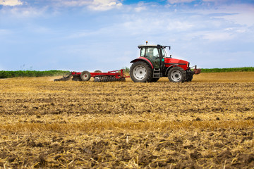 Naklejka premium Tractor cultivating wheat stubble field, crop residue.