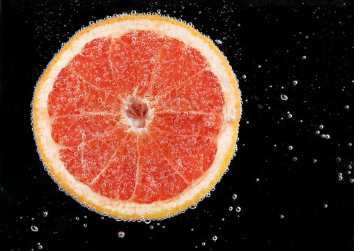 Fresh grapefruit in water with bubbles on black background