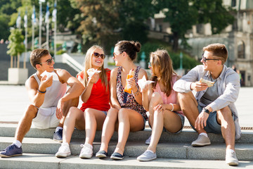 group of smiling friends sitting on city square