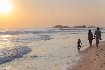 Family walking on sandy beach at sunset