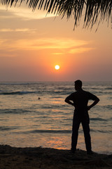 Silhouette  of a man standing on sandy beach at sunset.