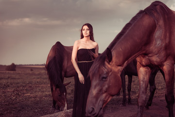 young woman and brown horses at grassland sunset