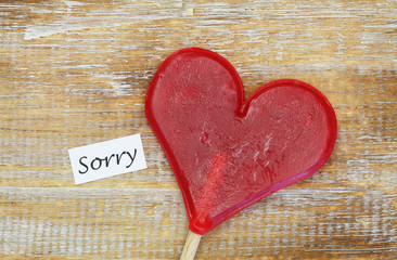Sorry card with heart shaped lollipop on wooden surface