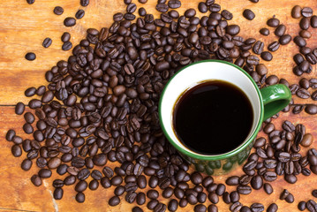 Cup of black coffee and coffee beans on wooden background.
