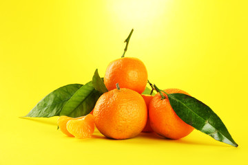 Ripe sweet tangerines with leaves, on yellow background