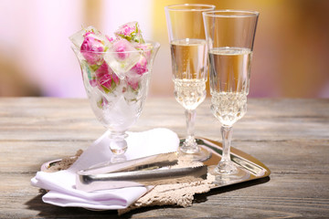 Ice cubes with rose flowers in glass bowl and two glasses with