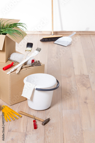 "Umzugskartons auf Parkett vor weißer Wand mit Werkzeug und Besen