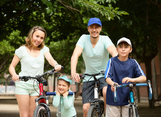happy family of four with bicycles and scooter