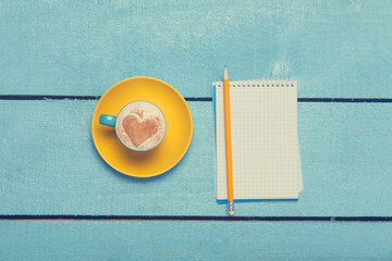 Cup of coffee with heart shape and pencil with notebook