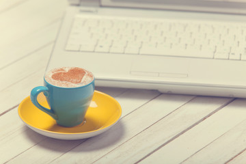 Cup of coffee with heart shape and notbook on wooden table.