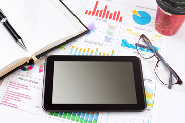 Business detail of a tablet lying on top of business charts