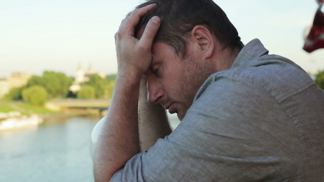 Sad man standing alone on the terrace and looking on the river