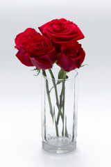 Cuatro rosas rojas dentro de vaso de cristal sobre una mesa roja