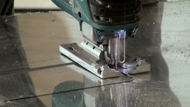 Sawing mirrored plastic using an electric jig saw. Closeup.