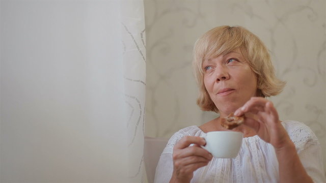 Senior woman sitting by the window drinking tea