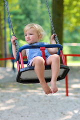Cute preschooler girl having fun on a swing on summer day