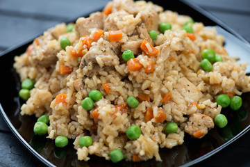 Pilaf with chicken, carrot and green peas on a black glass plate