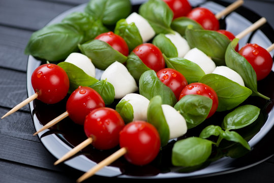 Kebabs with mozzarella, red tomatoes and green basil on a plate