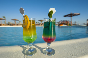 Two cocktail drinks by a tropical pool