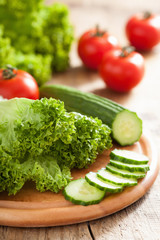 fresh cucumber tomatoes and salad leaves on chopping board