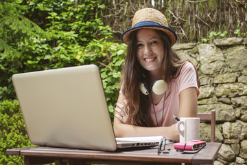 Young woman with straw hat working with laptop in outdoors.