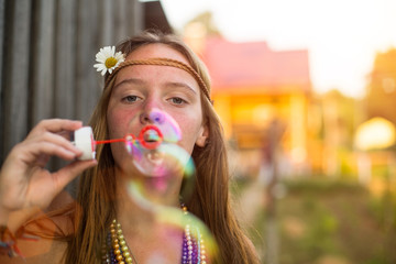 Young lovely hippie girl blow bubbles outdoors in village.