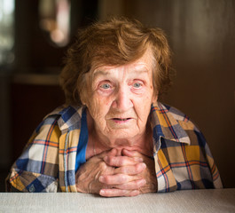 Close-up emotional old woman sitting at table in his house.