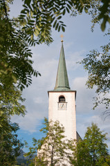 church spire against the cloudy sky surrounded by a tree