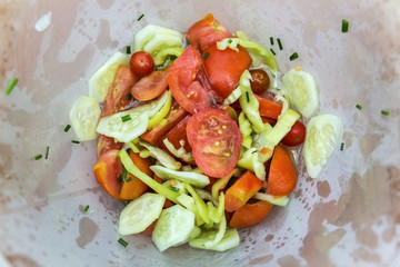 Cucumber, pepper and tomato salad with chives, in plastic bowl